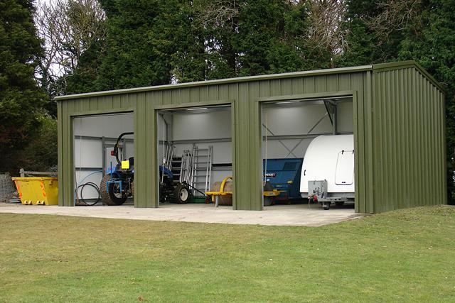 Farm machinery stored inside three open bays of a building