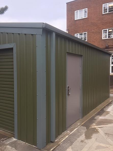 Close-up corner view of a green metal building showing the detail of the side personnel door and the ribbed cladding.